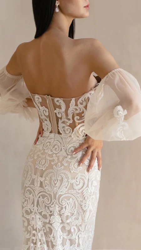 A woman in a wedding dress with sheer sleeves seen from behind.