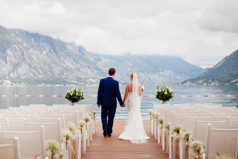 Bride and groom walking hand in hand on a lake dock.