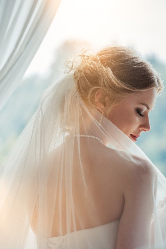 A bride in a beautiful dress stares pensively out the window.