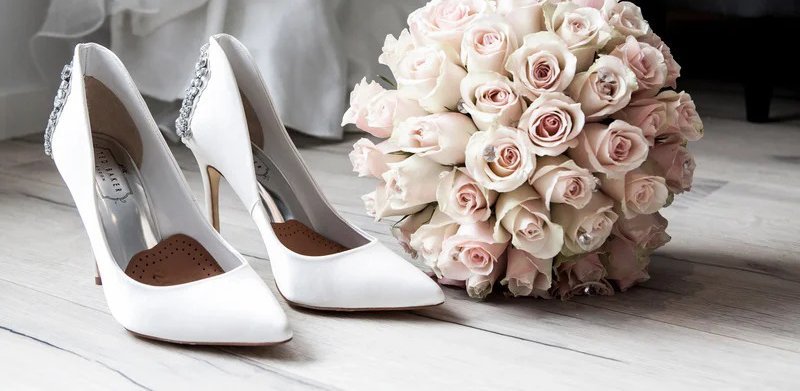 A bouquet of roses next to a pair of white shoes.