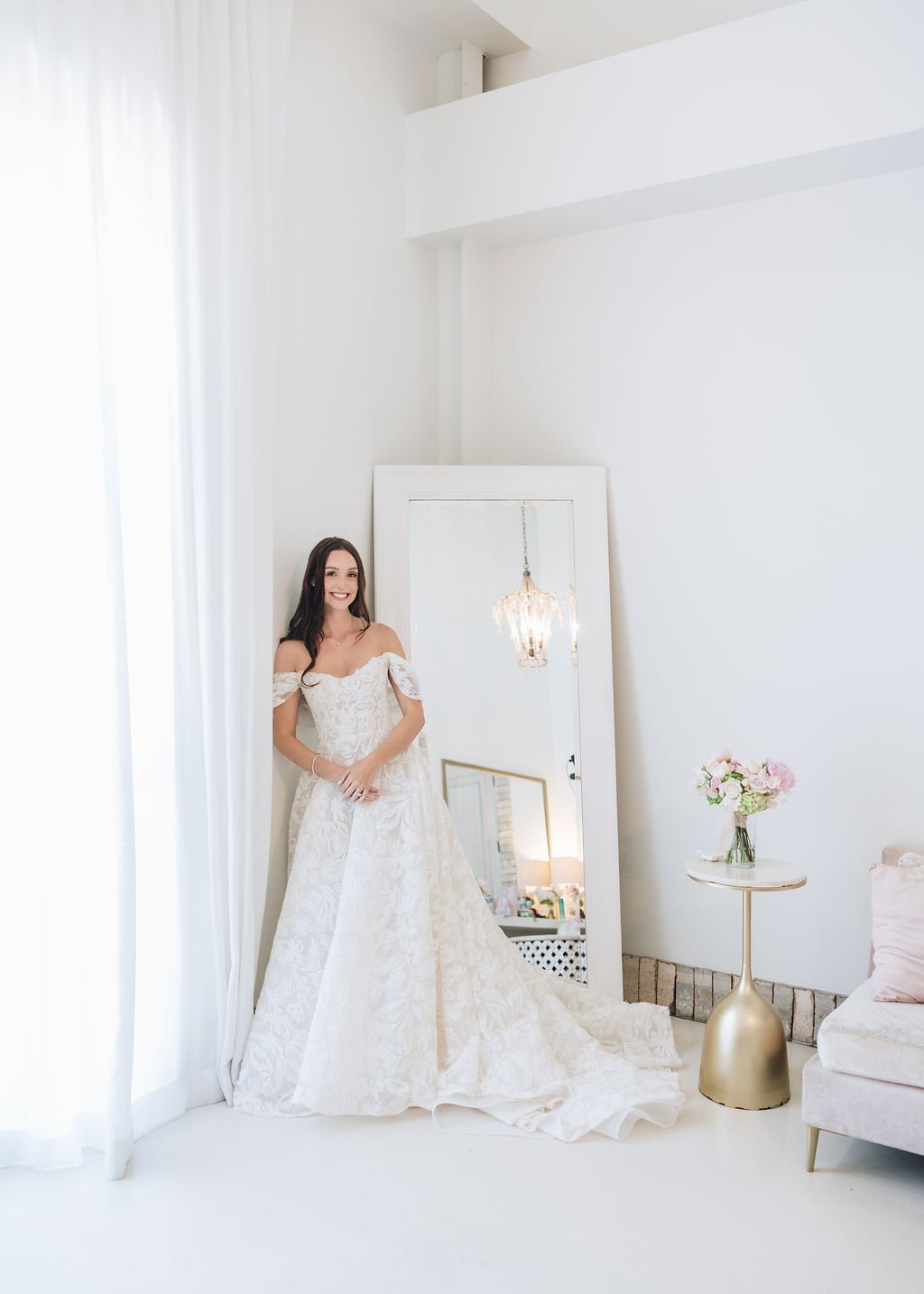 Bride in an off-the-shoulder lace gown beside a full-length mirror