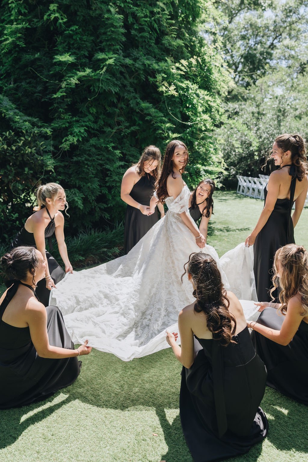 Bridesmaids in black dresses gathered around a bride and her train